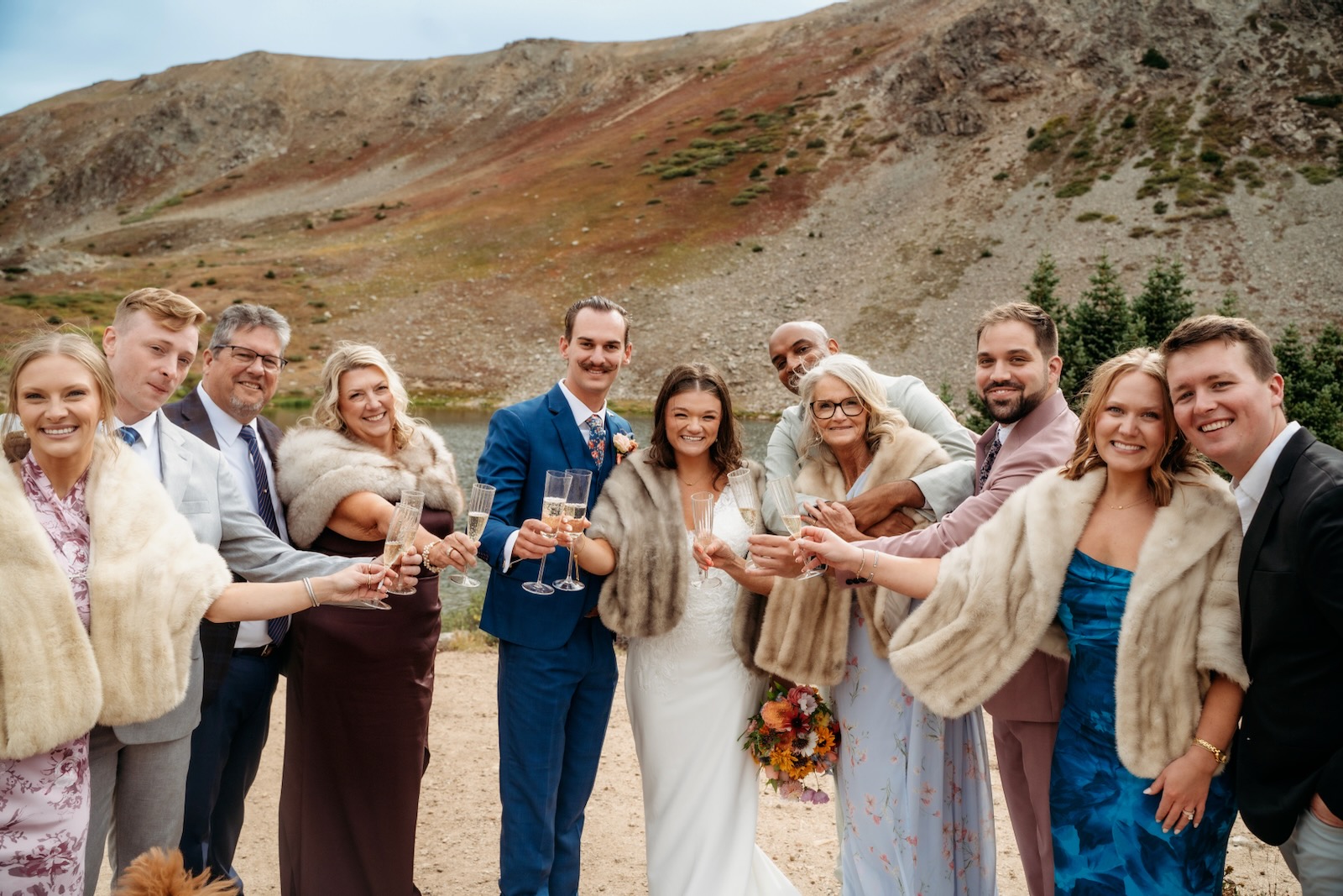 Wedding party toasting with champagne beside an alpine lake in Colorado